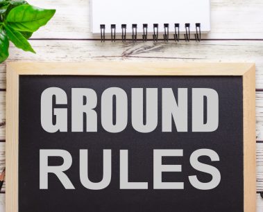 The word GROUND RULES written on a black background near pencils, a smartphone, a white notepad and a green plant in a pot